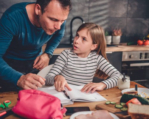 Father helping daughter with homework in kitchen Father helping daughter with homework on a dining table in kitchen